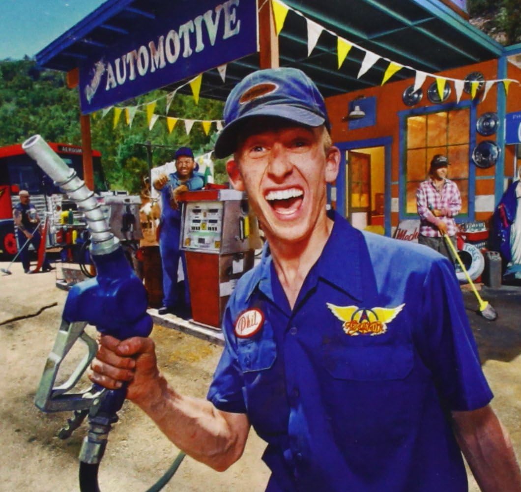 Mechanic holding a gas pump in front of a gas station with 'Automotive' sign.