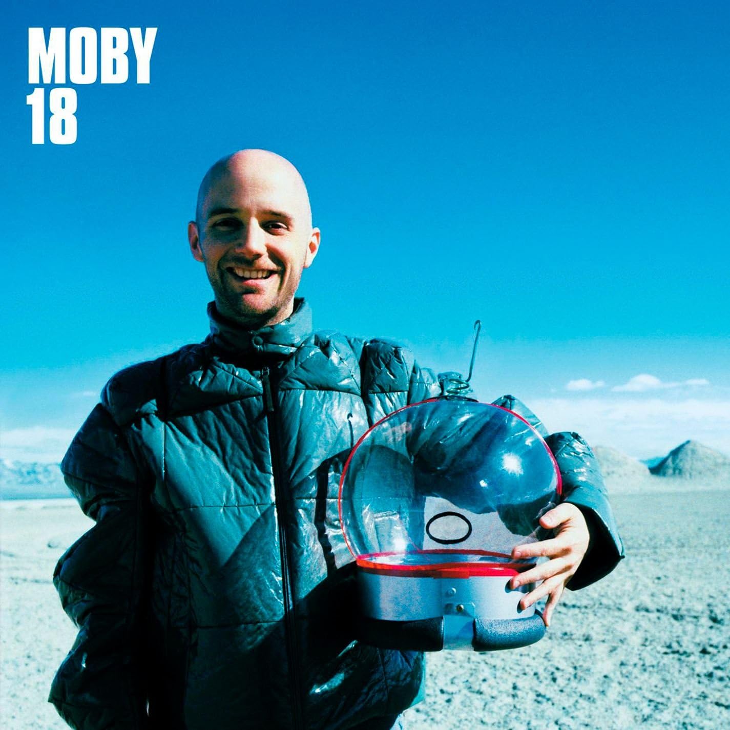 Person holding a transparent sphere with red rim against a blue sky and desert landscape, featuring 'Moby 18' text.