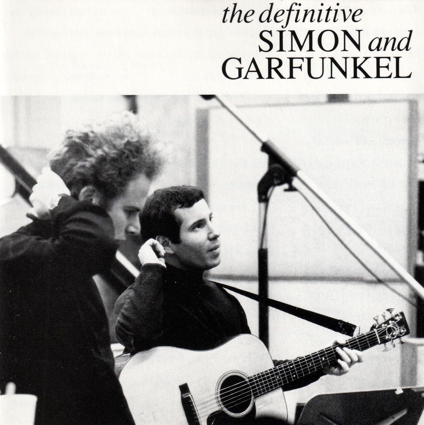 Black and white photo of two musicians in a studio with text 'the definitive SIMON and GARFUNKEL'.