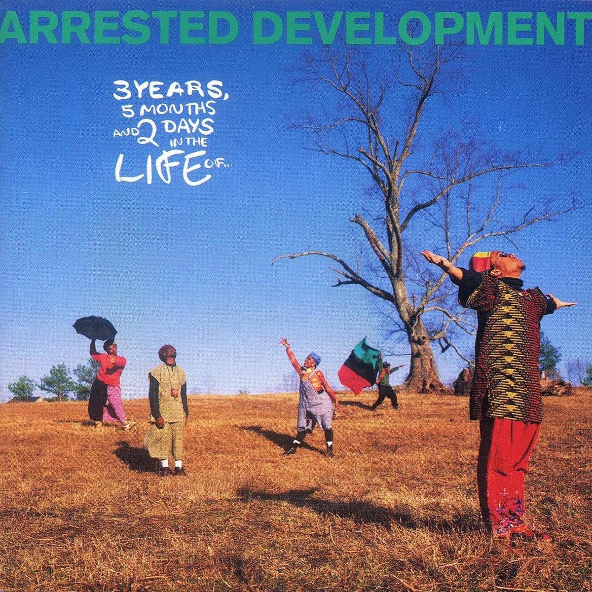 Album cover art for 'Arrested Development' featuring a group of people in colorful clothing on a dry grassy field under a bright blue sky, with a large leafless tree in the background. The title 'ARRESTED DEVELOPMENT' is written in green at the top, and '3 YEARS, 5 MONTHS AND 2 DAYS IN THE LIFE U.