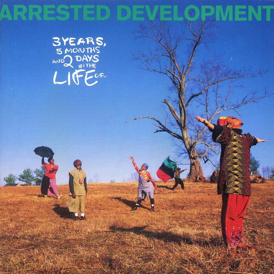 Album cover art for 'Arrested Development' featuring a group of people in colorful clothing on a dry grassy field under a bright blue sky, with a large leafless tree in the background. The title 'ARRESTED DEVELOPMENT' is written in green at the top, and '3 YEARS, 5 MONTHS AND 2 DAYS IN THE LIFE U.