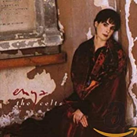 The cover image shows the artist Enya, prominently featured, with a backdrop of an old, textured wall. She is wearing a red and brown outfit and posing in a thoughtful, seated posture.