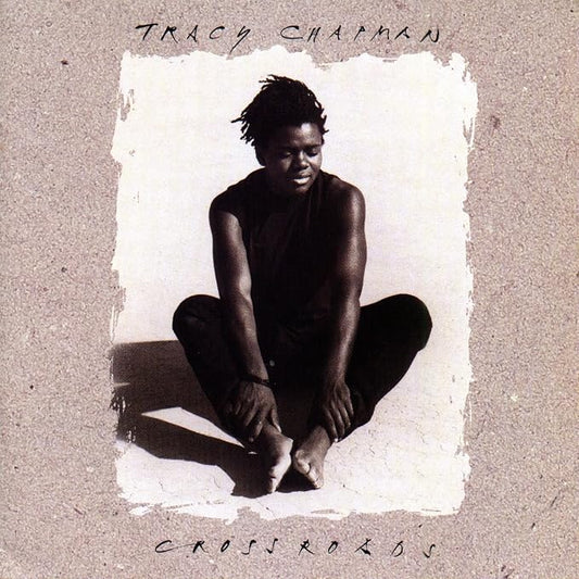Album cover for Tracy Chapman's 'Crossroads', featuring a black-and-white portrait of the artist sitting cross-legged against a textured beige background with handwritten text.