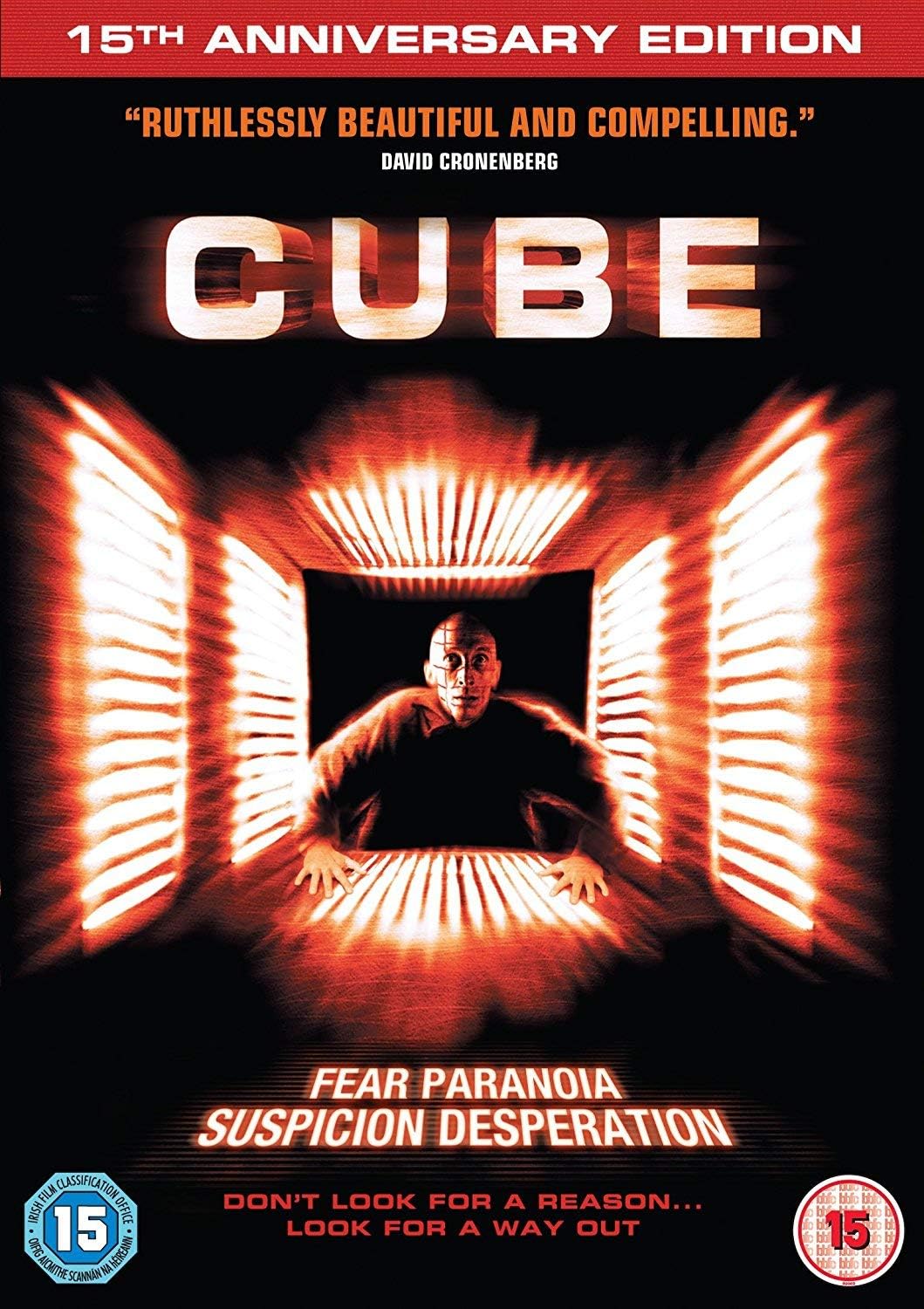 15th Anniversary Edition DVD cover for the film 'Cube', featuring a dark background with a glowing orange-red tunnel effect, the title 'CUBE' in large metallic letters, and a central figure looking forward. Text includes 'Fear Paranoia Suspicion Desperation' and age rating badges in the corners.