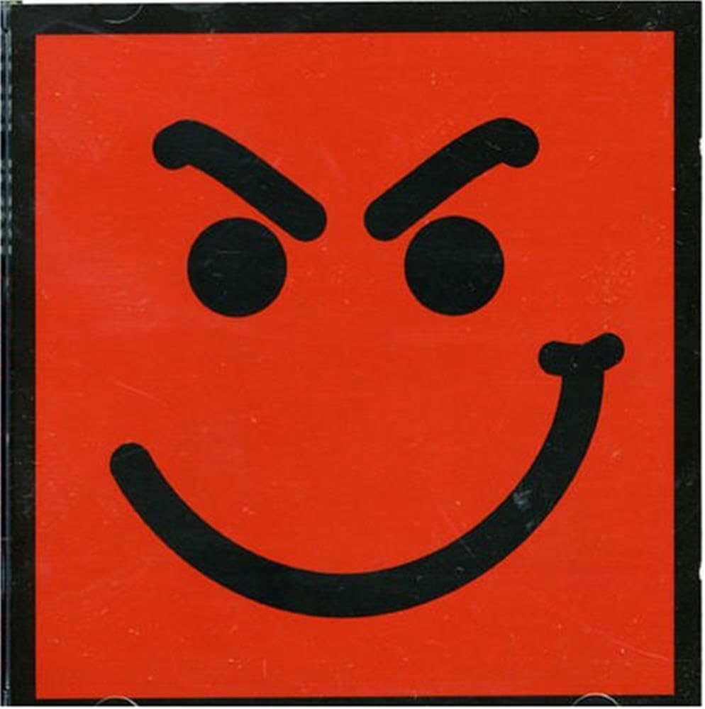 A square red sign or sticker featuring a black angry face with thick black eyebrows, circular eyes, and a wide curved smile, bordered by a black frame.