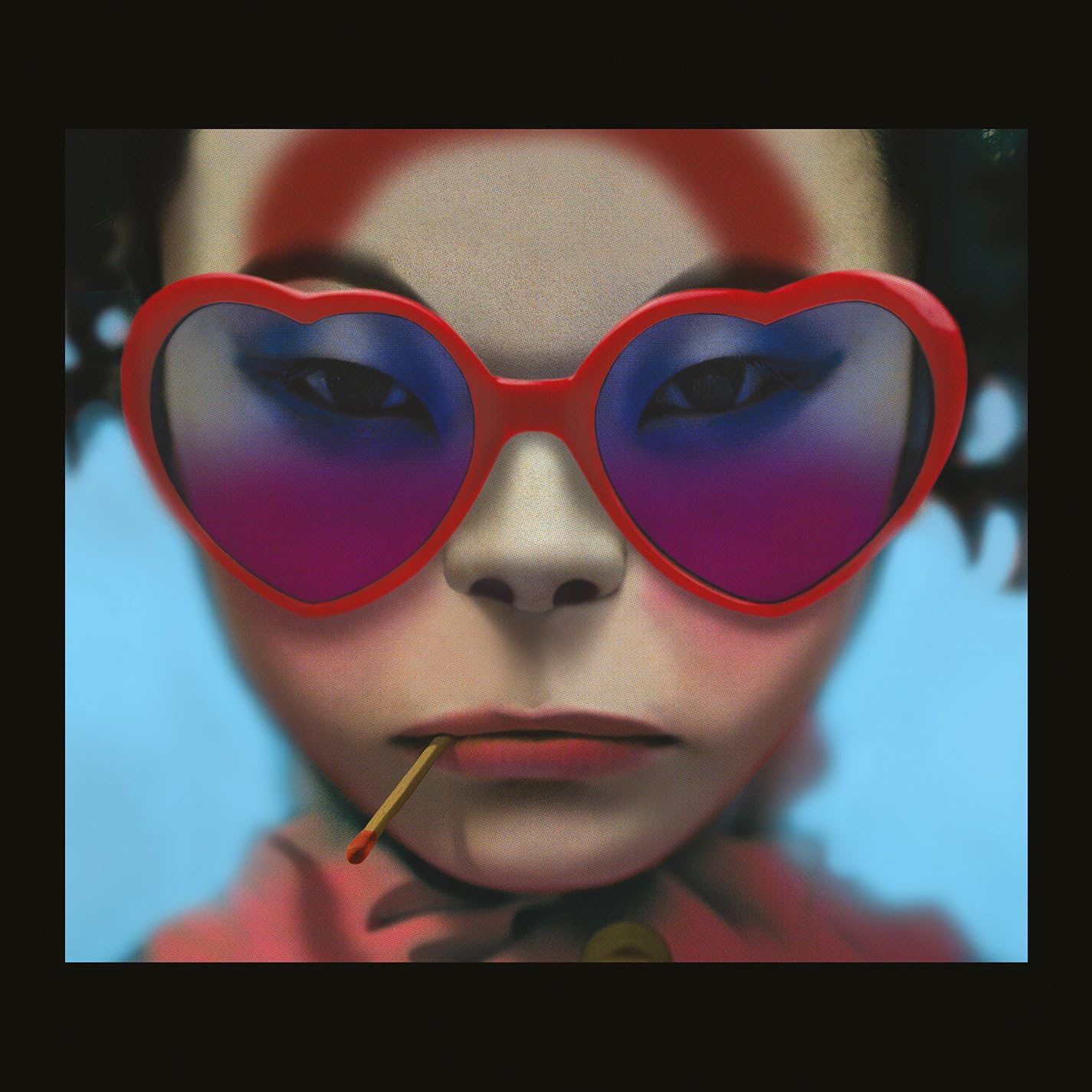Person wearing heart-shaped sunglasses with a blue gradient, holding a toothpick.