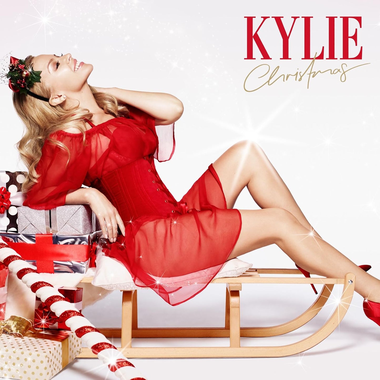 Woman in a red dress sitting on a sled with Christmas decorations, featuring the Kylie brand.
