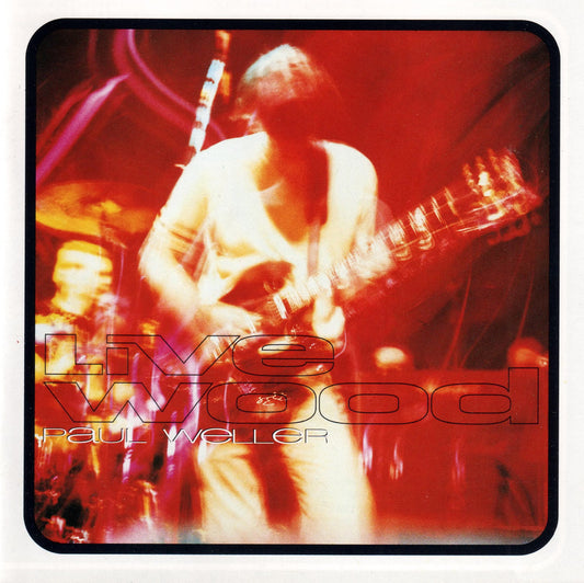 Album cover for Paul Weller's 'Live Wood' featuring a blurred live performance photo of the musician playing guitar on a red-lit stage, with the title and artist name overlaid in large stylized text.
