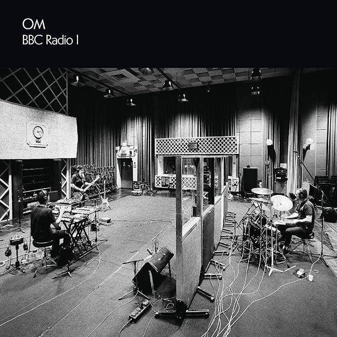 A black and white photo of a band performing in a studio setting, with equipment and a audience in the background, indicating a live radio broadcast.