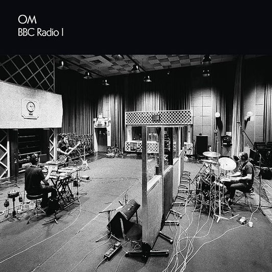 A black and white photo of a band performing in a studio setting, with equipment and a audience in the background, indicating a live radio broadcast.