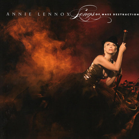 Annie Lennox 'Songs of Mass Destruction' album cover featuring the artist in a black hat and dark dress posed against a smoky orange and black background, with the album title and artist name printed at the top.