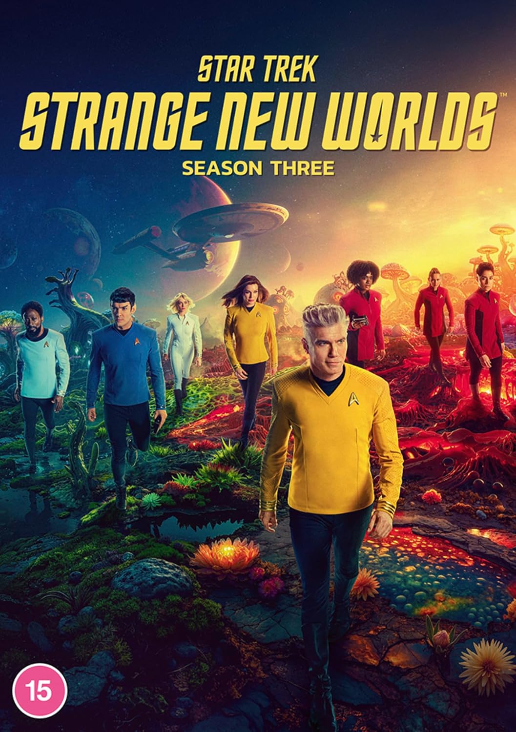 Star Trek: Strange New Worlds Season Three cover art featuring the cast walking across a colorful alien landscape with a spaceship and planet in the background. Large yellow title text appears at the top, with a pink 15 rating badge in the lower left corner.