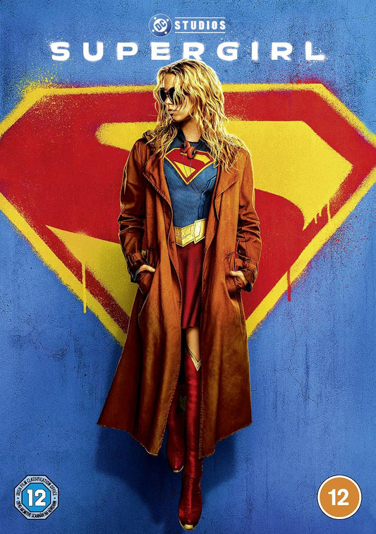 DC Studios Supergirl poster featuring a woman in a brown trench coat over a blue, red, and yellow costume, standing in front of a large red and yellow Superman-style shield on a blue background.