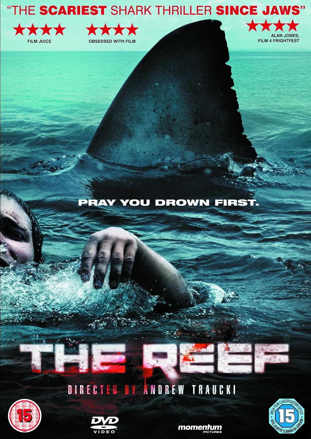 Movie poster for the 2005 film 'The Reef' directed by Andrew Traucki, featuring a shark fin and a person's arm and head emerging from turquoise ocean water. The title 'THE REEF' appears in large distressed white and red letters at the bottom, with DVD and 15 rating logos visible.