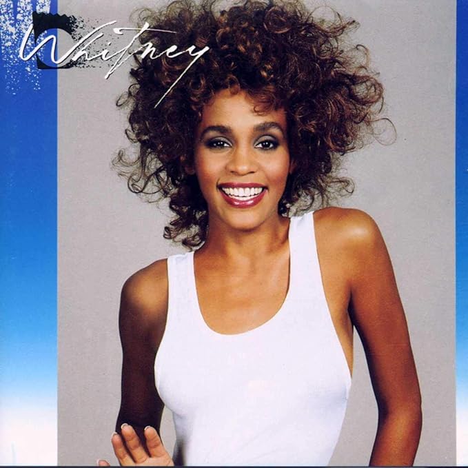 Whitney Houston's album cover featuring a young woman with curly hair, smiling, against a blue background.