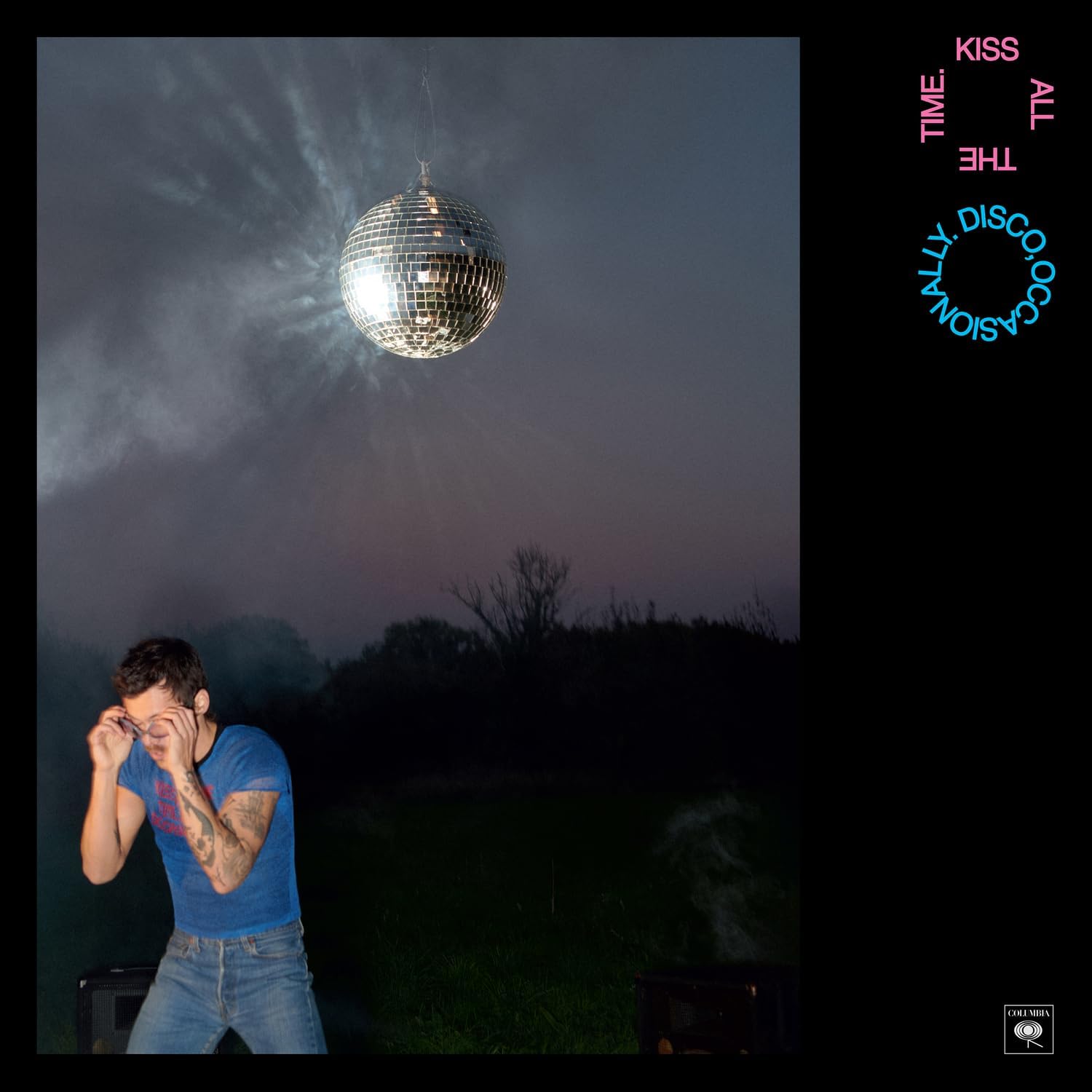 Person in a blue shirt standing under a disco ball in a dark outdoor setting