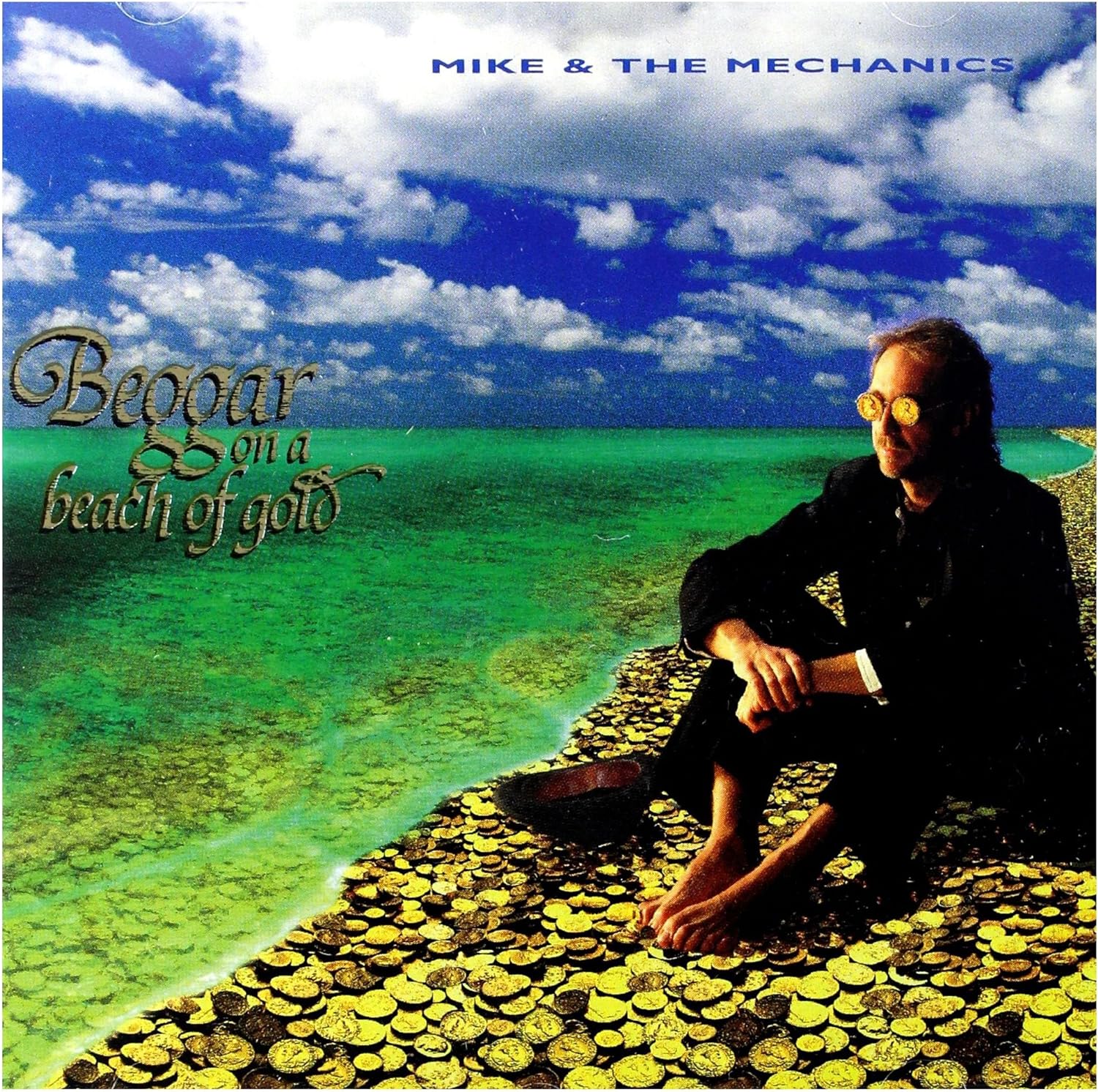 The cover of the Mike & The Mechanics album 'Beggar On A Beach Of Gold' features a man sitting on a beach with a clear blue sky and yellow sand in the background. The artist's name and the title of the album are prominently displayed.